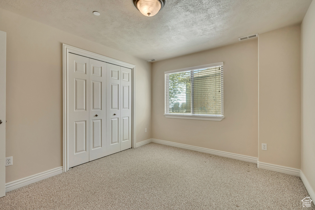 Unfurnished bedroom featuring carpet, a textured ceiling, a closet, and baseboards