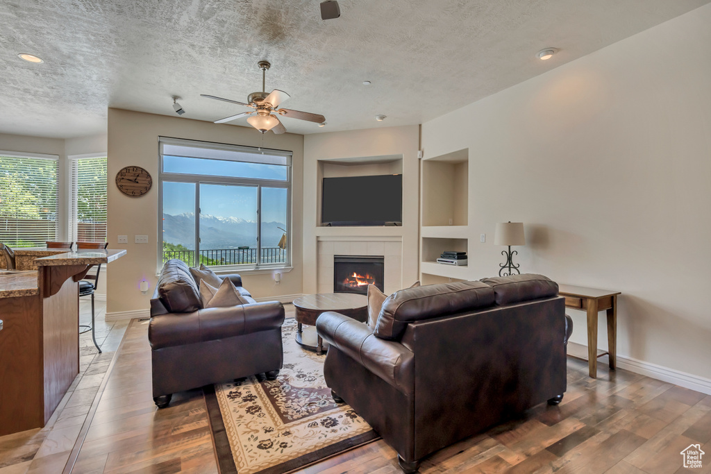 Living room with light wood-type flooring, a textured ceiling, a fireplace, built in shelves, and baseboards