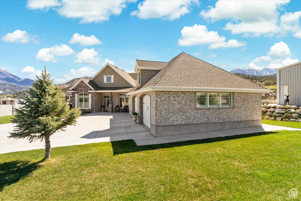 Rear view of property with brick siding, a mountain view, driveway, and a yard