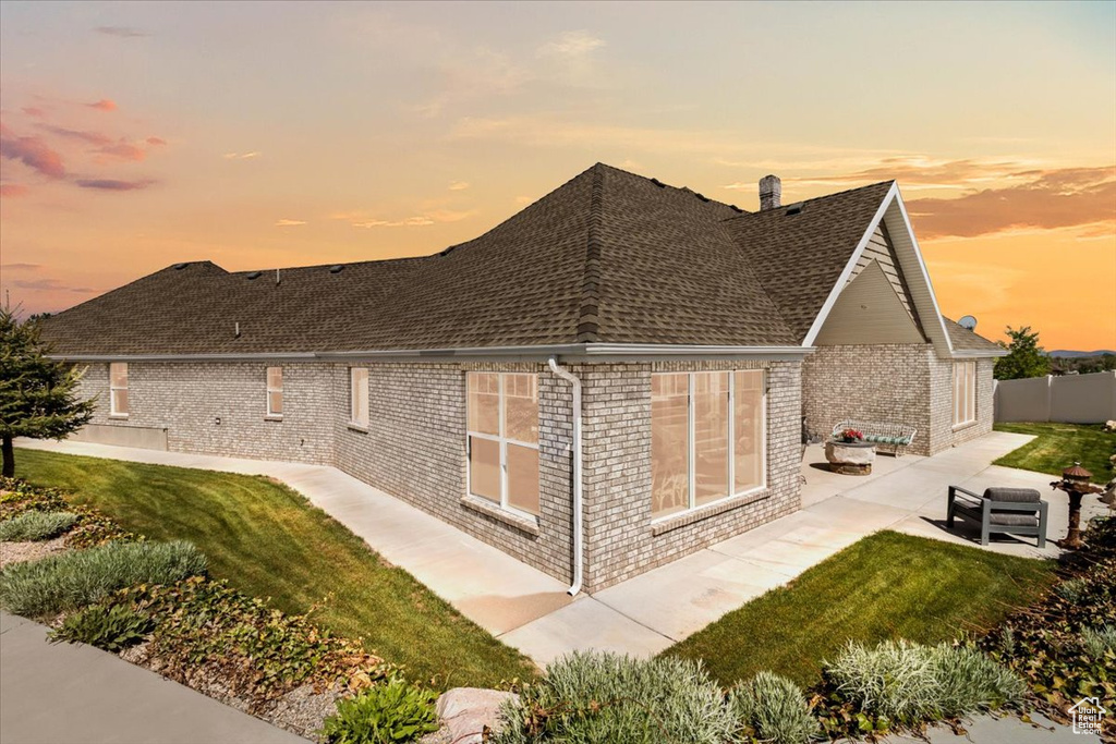 Property exterior at dusk with brick siding, a patio, and roof with shingles