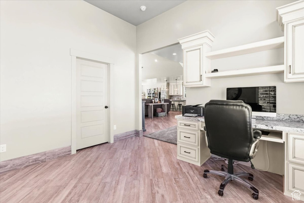 Home office featuring light wood-style flooring, built in study area, and a towering ceiling