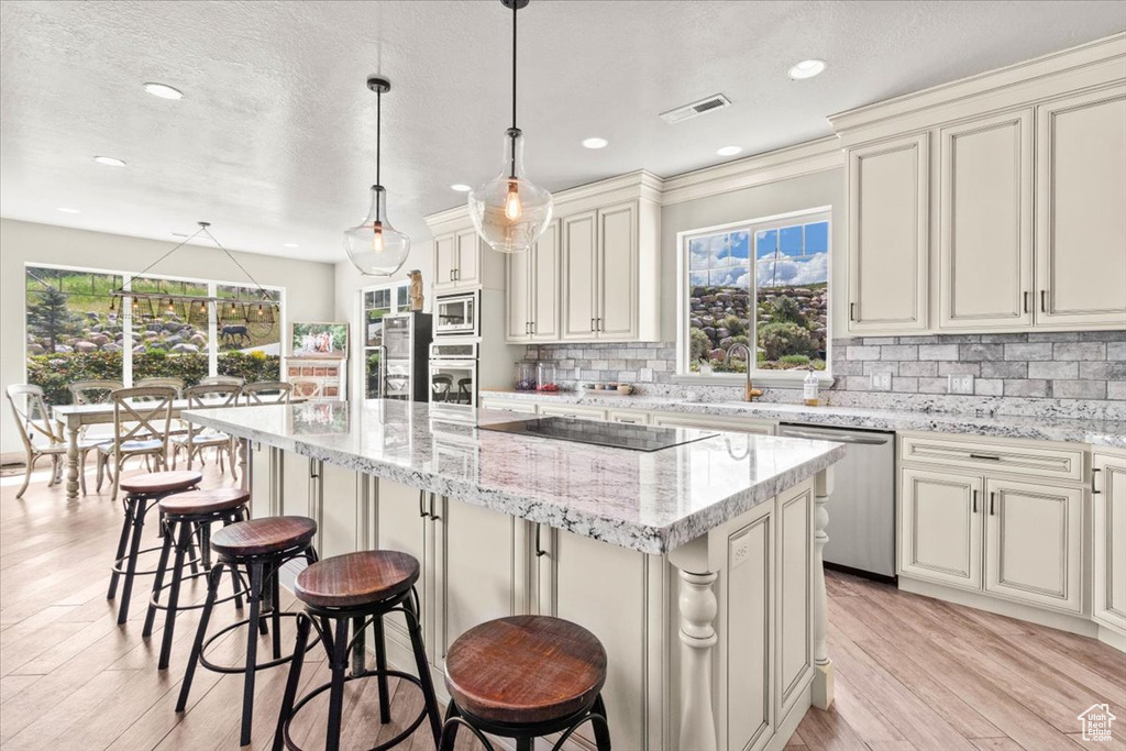 Kitchen featuring appliances with stainless steel finishes, a sink, a kitchen island, light wood-style floors, and tasteful backsplash