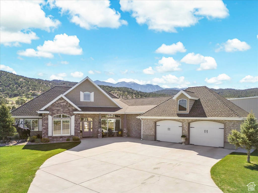 View of front facade featuring a mountain view, a front yard, concrete driveway, brick siding, and a garage