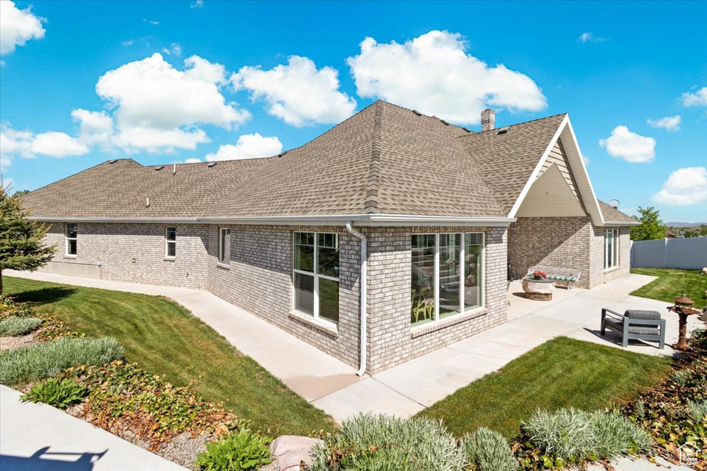 Back of property featuring a patio area, roof with shingles, brick siding, and a chimney