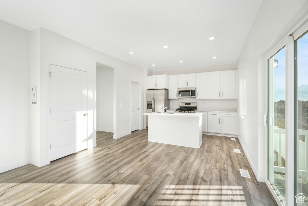 Kitchen with stainless steel appliances, light wood-style floors, baseboards, white cabinetry, and recessed lighting