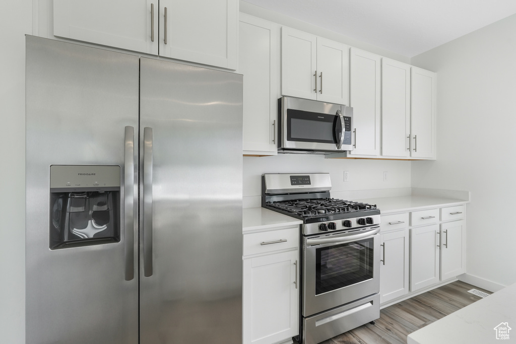 Kitchen with stainless steel appliances, light wood finished floors, and white cabinetry