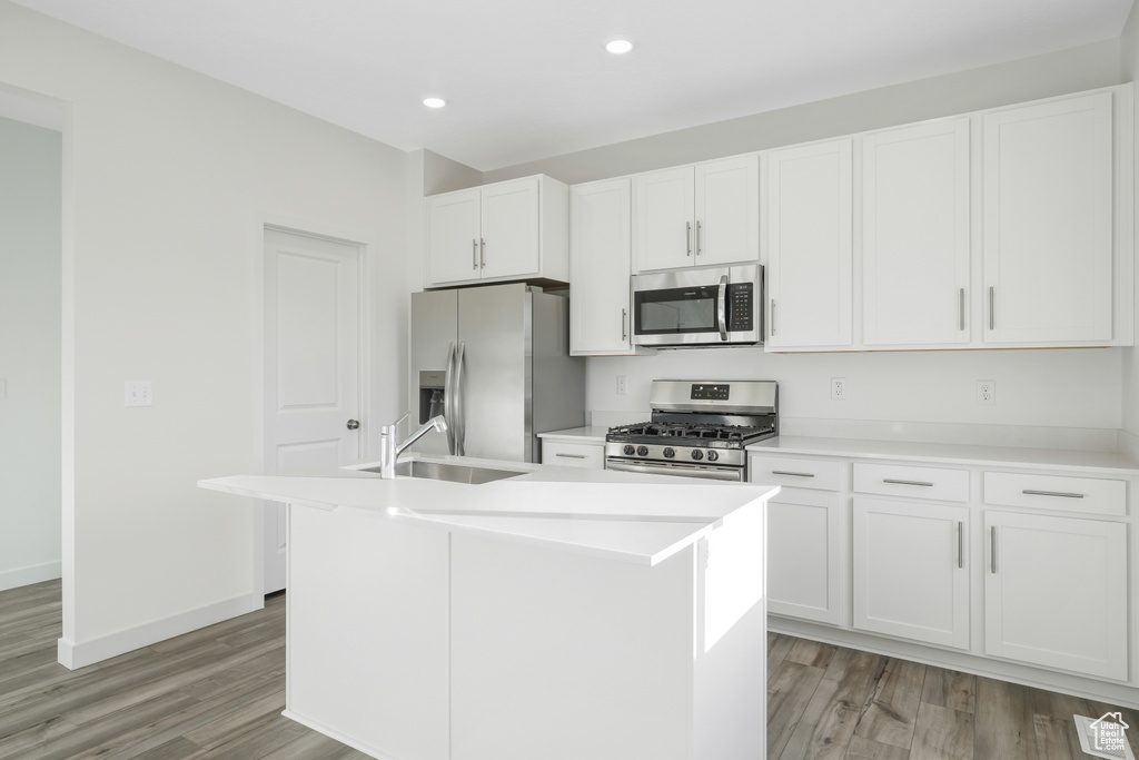 Kitchen with appliances with stainless steel finishes, a sink, light wood-style floors, a kitchen island with sink, and white cabinets