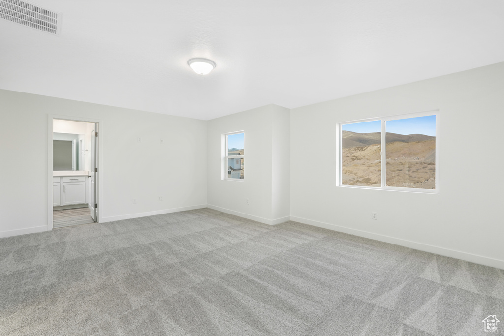 Unfurnished bedroom with light carpet, multiple windows, baseboards, and connected bathroom