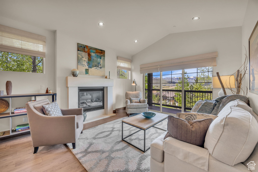 Living room with a glass covered fireplace, lofted ceiling, recessed lighting, and wood finished floors