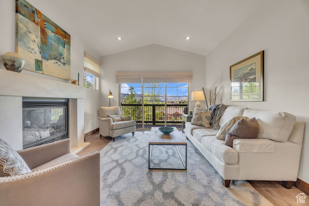Living room with wood finished floors, vaulted ceiling, plenty of natural light, a glass covered fireplace, and baseboards