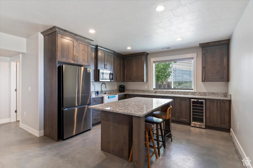 Kitchen featuring stainless steel appliances, beverage cooler, concrete flooring, a breakfast bar area, and recessed lighting