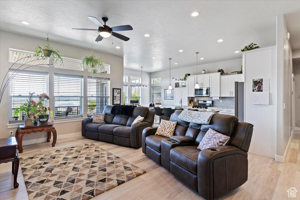 Living area with ceiling fan, recessed lighting, light wood-type flooring, baseboards, and a textured ceiling