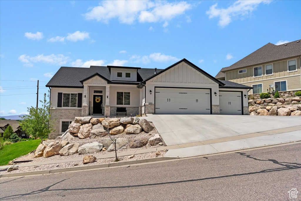 Modern farmhouse with a garage, stone siding, driveway, and board and batten siding