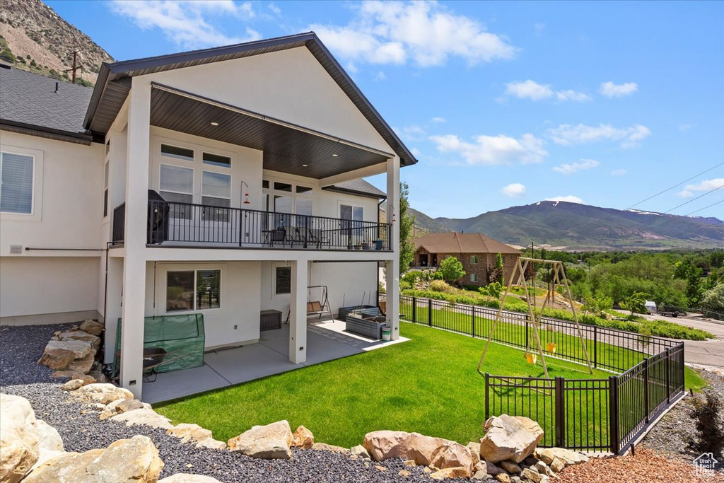 Back of property with a balcony, a mountain view, a patio area, and stucco siding