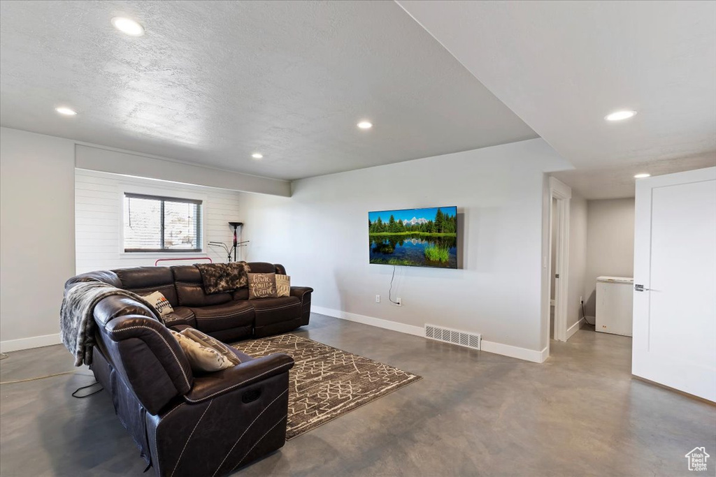 Living room featuring concrete flooring, baseboards, recessed lighting, and a textured ceiling