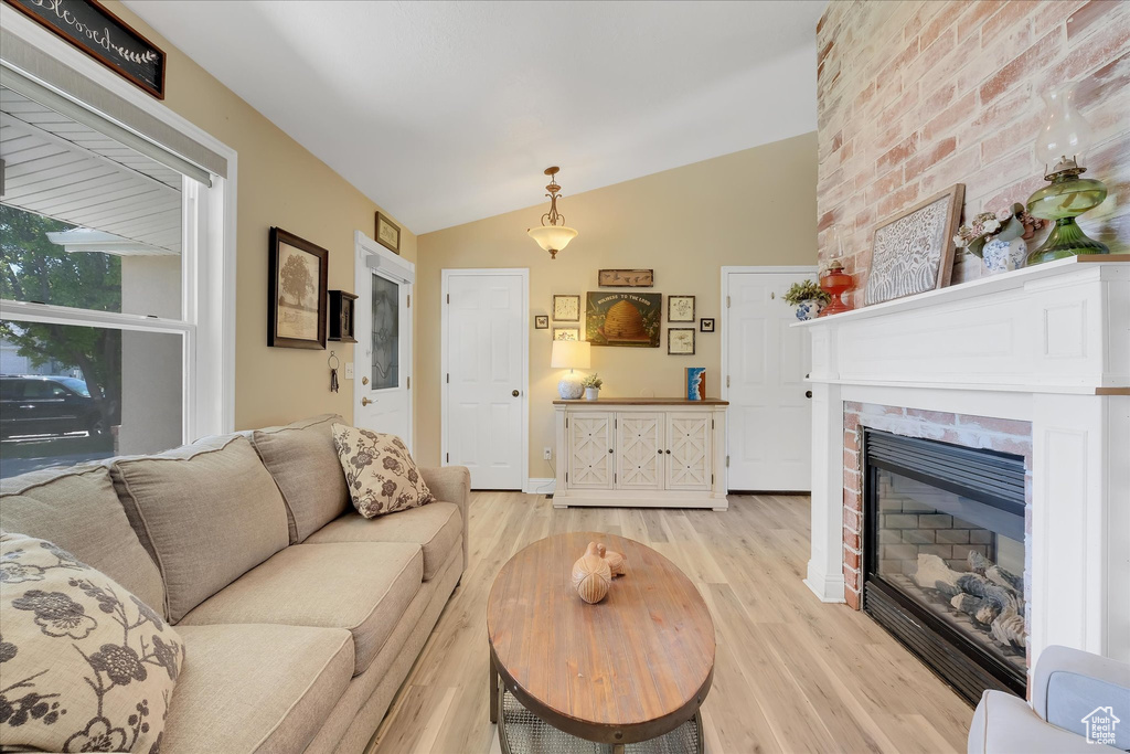Living room with light wood finished floors, vaulted ceiling, and a brick fireplace