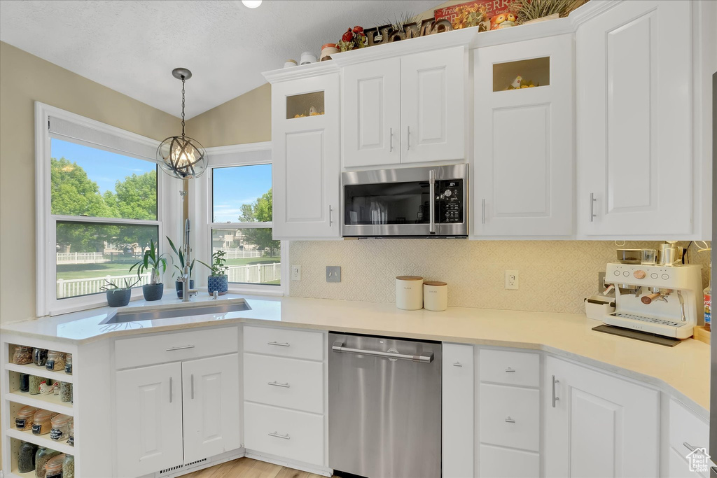 Kitchen with stainless steel appliances, a sink, decorative backsplash, white cabinetry, and lofted ceiling