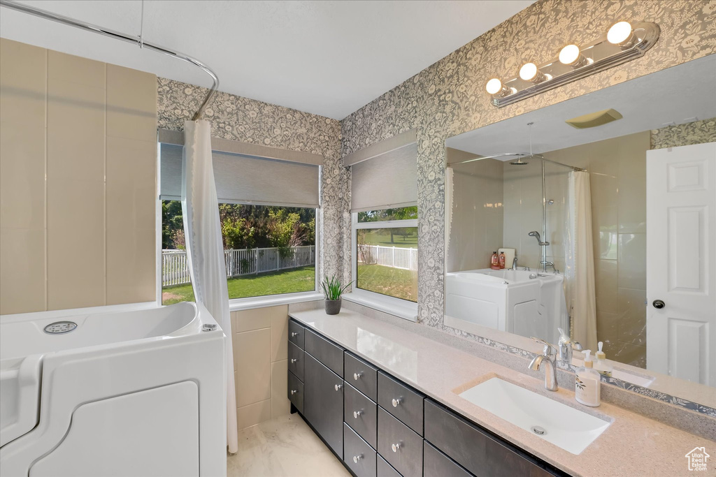 Bathroom featuring a shower with shower curtain, vanity, washer / dryer, and a bathtub