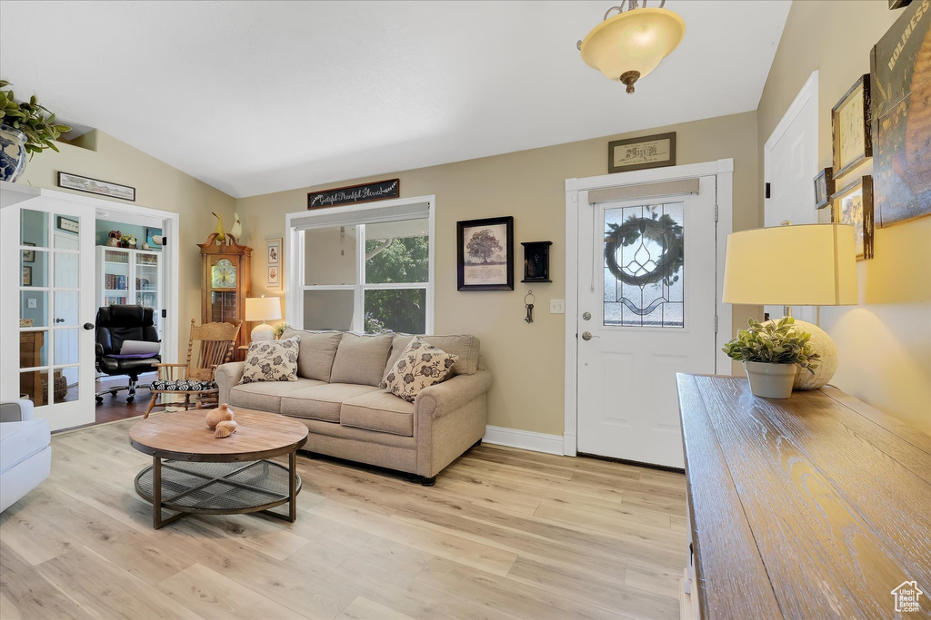 Living area featuring plenty of natural light, light wood finished floors, lofted ceiling, baseboards, and french doors