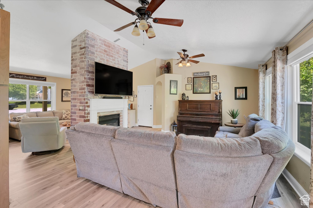 Living area featuring lofted ceiling, ceiling fan, light wood-style floors, and healthy amount of natural light