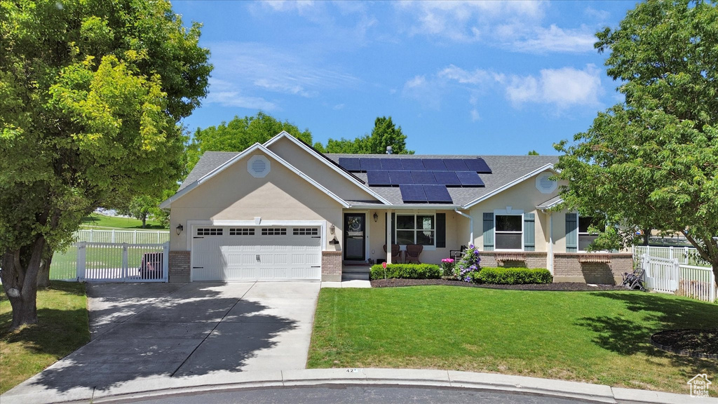 Single story home with brick siding, an attached garage, concrete driveway, roof mounted solar panels, and roof with shingles