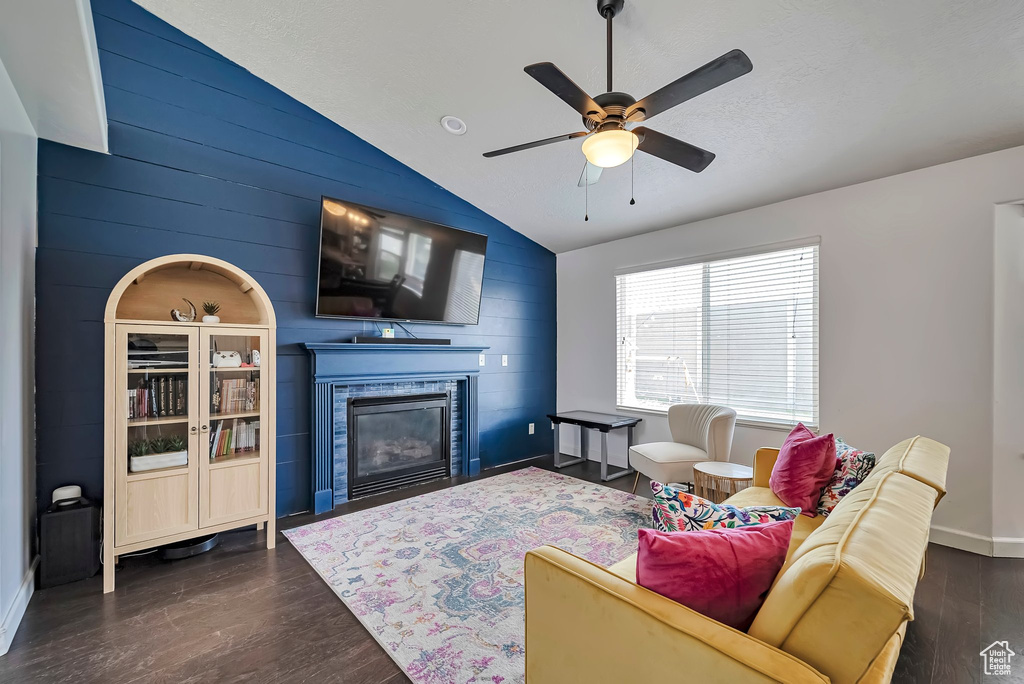Living room featuring lofted ceiling, a ceiling fan, dark wood-style flooring, baseboards, and a glass covered fireplace