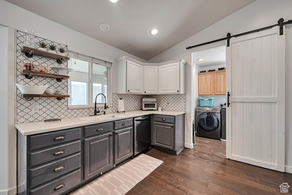 Kitchen with a sink, washer and clothes dryer, dishwasher, lofted ceiling, and a barn door
