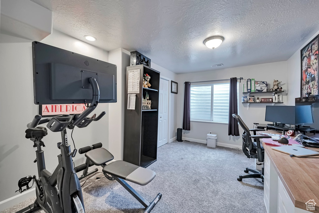 Carpeted home office featuring a textured ceiling and baseboards