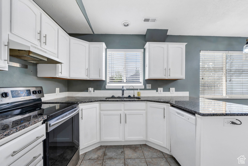 Kitchen with electric stove, a sink, under cabinet range hood, dishwasher, and white cabinets