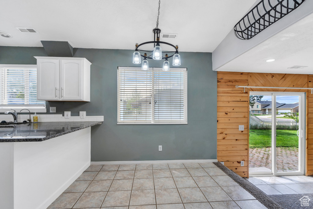 Kitchen with white cabinetry, baseboards, dark stone counters, light tile patterned floors, and a chandelier