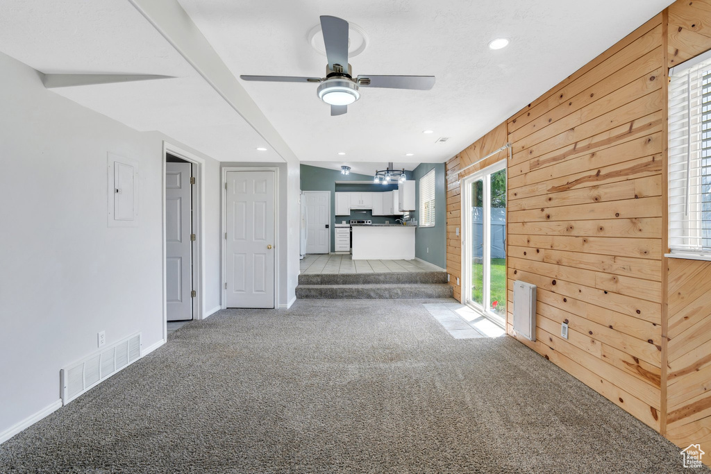 Unfurnished living room featuring light carpet, ceiling fan, wooden walls, baseboards, and electric panel