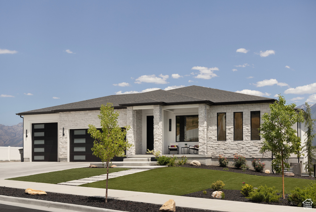 View of front of house with an attached garage, driveway, a front lawn, a porch, and stone siding