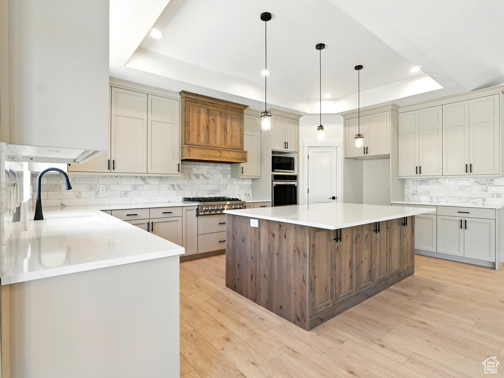 Kitchen featuring stainless steel appliances, a raised ceiling, a sink, backsplash, and a kitchen island