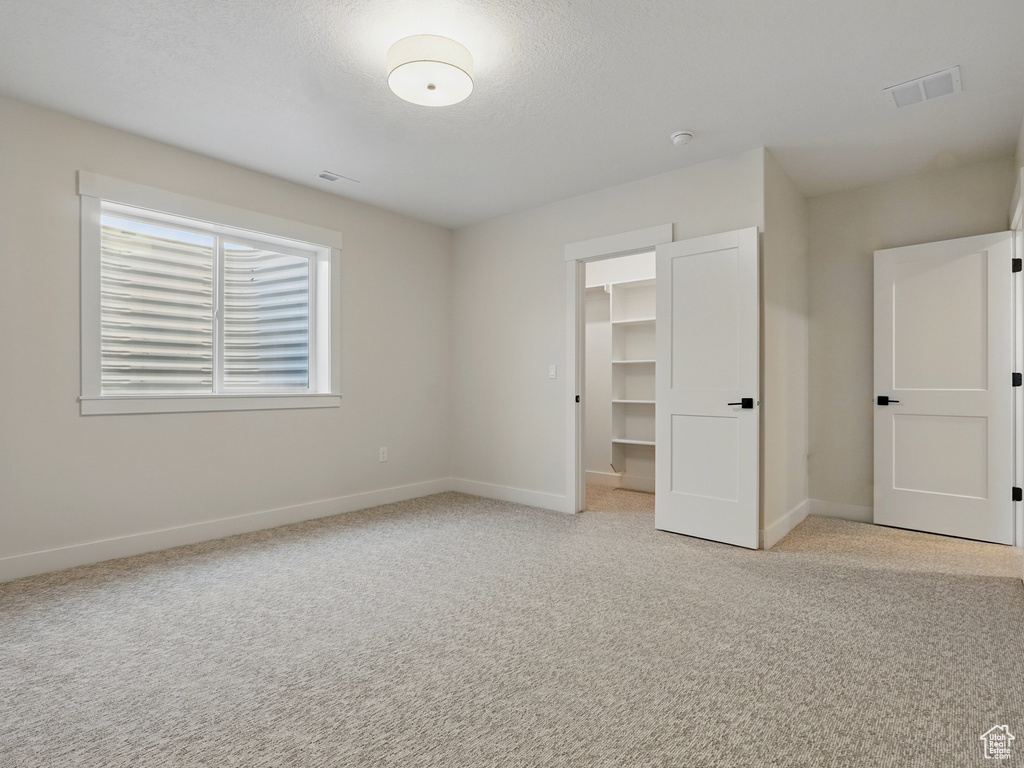 Unfurnished bedroom featuring light carpet, a walk in closet, baseboards, and a closet