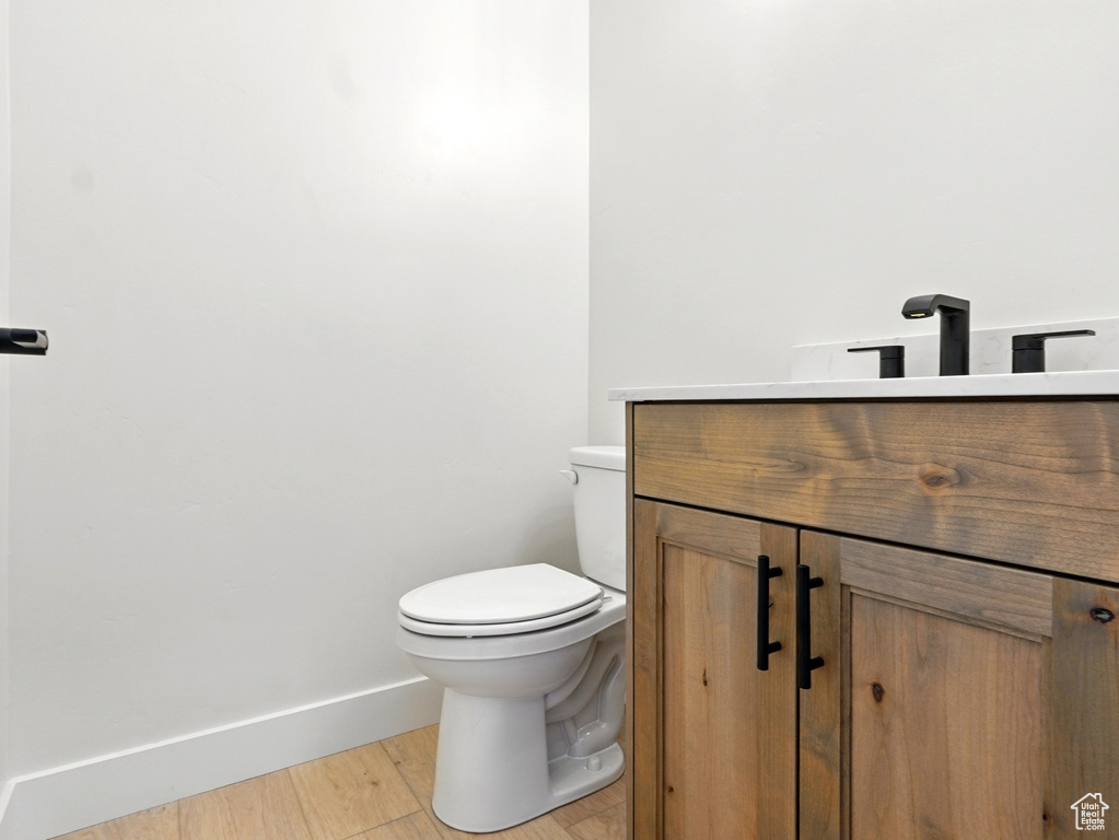 Half bath with vanity, toilet, baseboards, and wood finished floors
