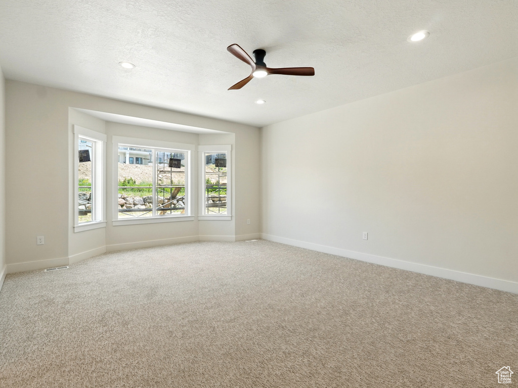 Unfurnished room with light colored carpet, ceiling fan, baseboards, recessed lighting, and a textured ceiling
