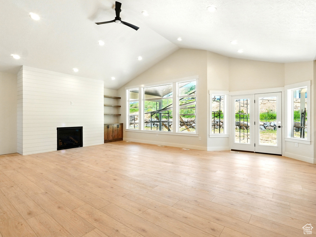 Unfurnished living room featuring a fireplace, ceiling fan, high vaulted ceiling, light wood-type flooring, and baseboards