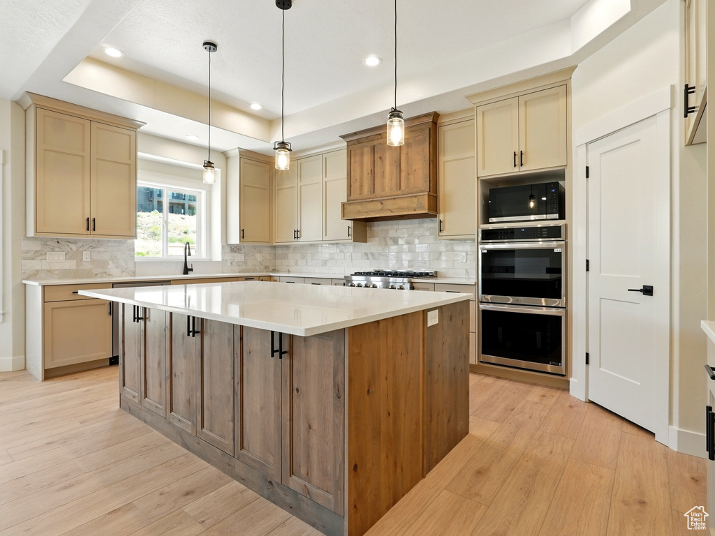 Kitchen featuring appliances with stainless steel finishes, a raised ceiling, light wood-style floors, a kitchen island, and recessed lighting