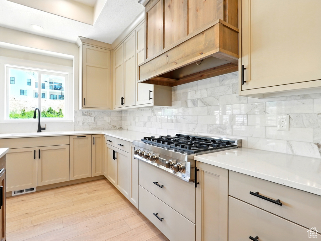 Kitchen featuring a sink, stainless steel gas stovetop, under cabinet range hood, and backsplash