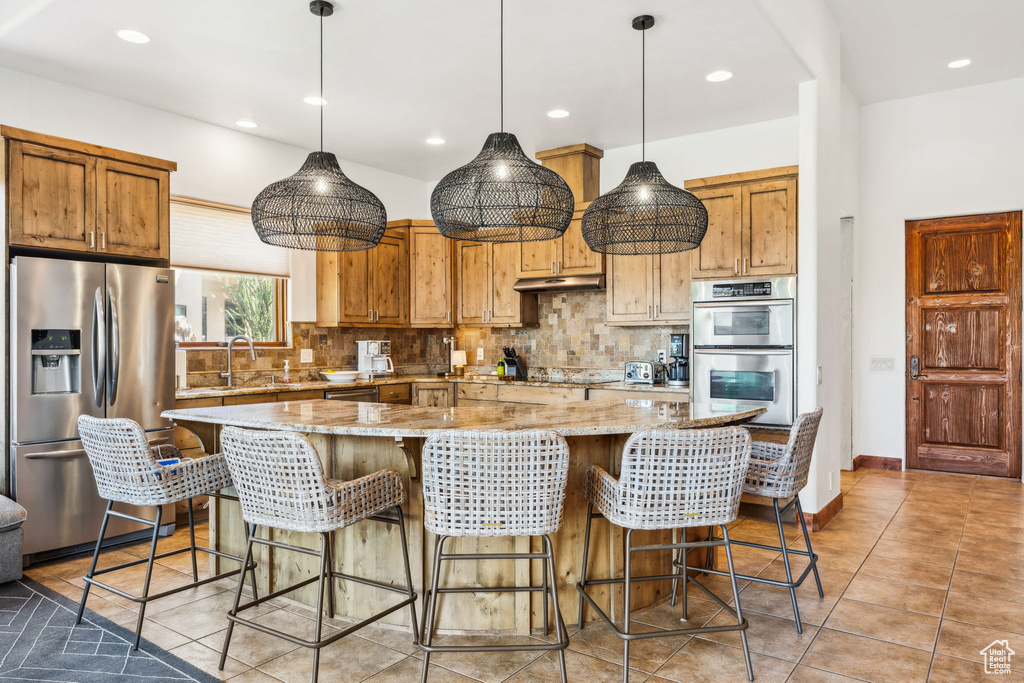 Kitchen with stainless steel appliances, under cabinet range hood, decorative backsplash, a large island, and light stone countertops