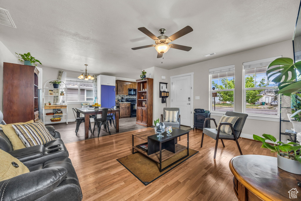 Living room featuring light wood-type flooring, a chandelier, ceiling fan, and baseboards