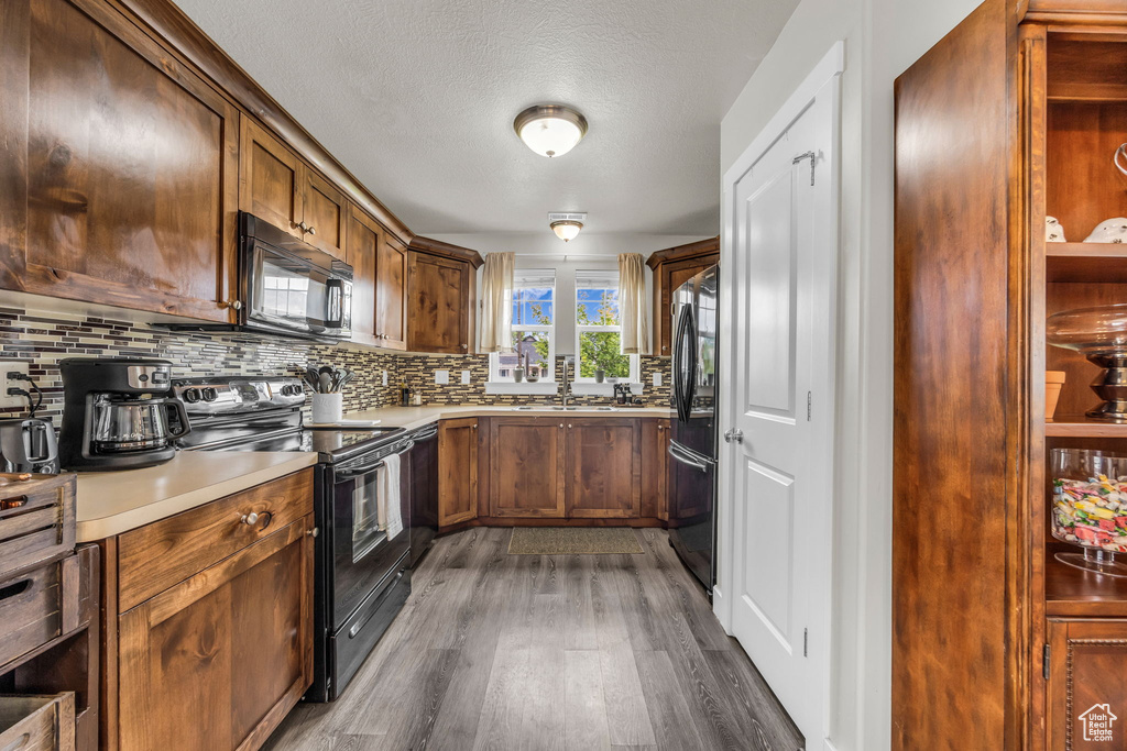Kitchen with black appliances, dark wood-type flooring, backsplash, a sink, and light countertops