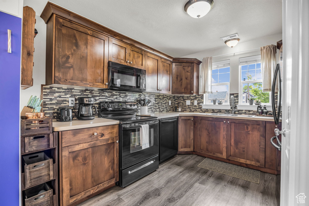 Kitchen with black appliances, a sink, wood finished floors, and decorative backsplash