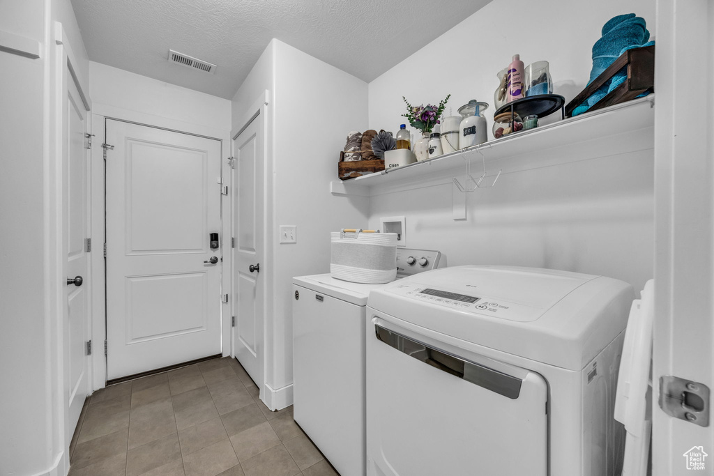 Laundry area featuring washer and clothes dryer, light tile patterned floors, and a textured ceiling