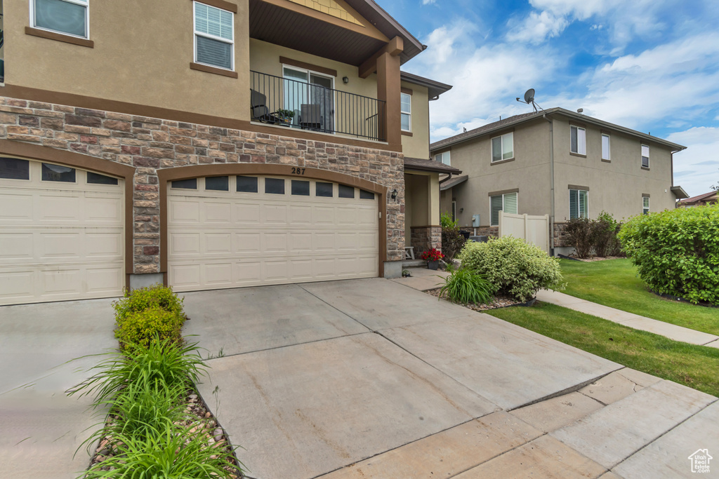 Townhome / multi-family property featuring stone siding, stucco siding, a garage, a balcony, and concrete driveway