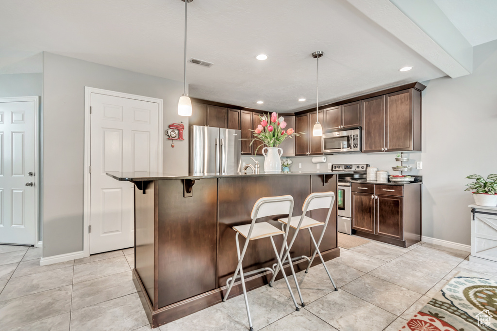 Kitchen with stainless steel appliances, a kitchen breakfast bar, light tile patterned flooring, dark brown cabinets, and recessed lighting