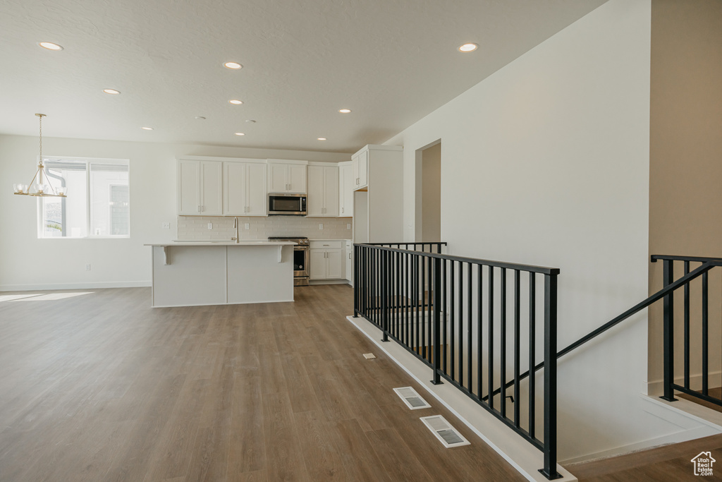 Kitchen with appliances with stainless steel finishes, wood finished floors, white cabinetry, decorative backsplash, and recessed lighting