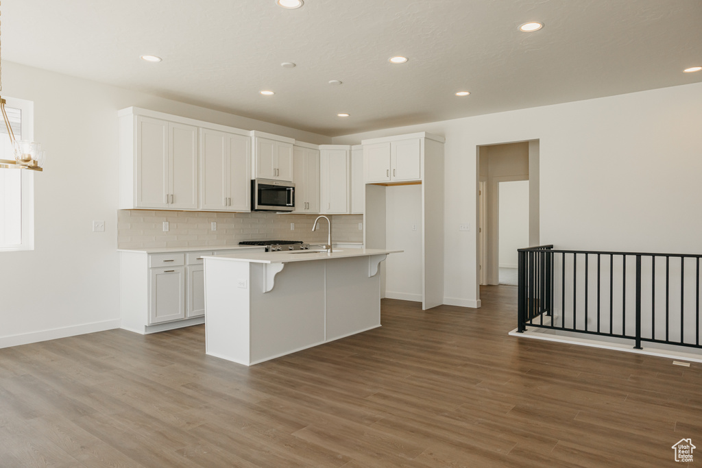 Kitchen featuring stainless steel microwave, decorative backsplash, light countertops, light wood-type flooring, and white cabinetry