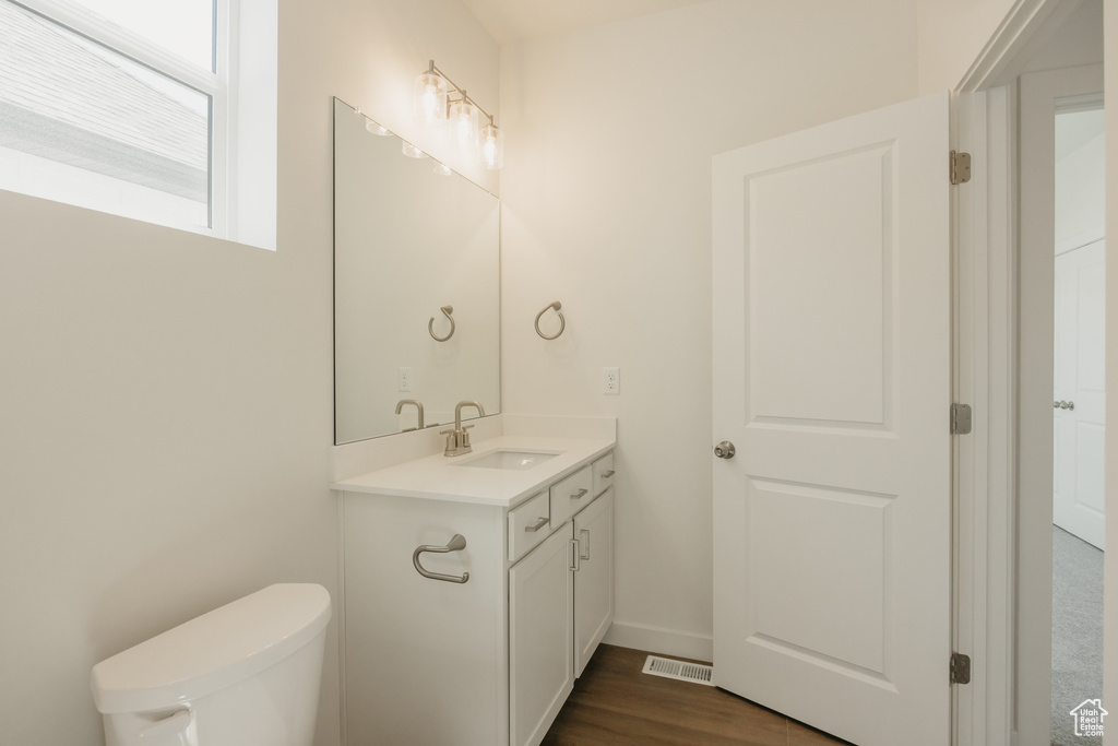 Half bath with vanity, toilet, wood finished floors, and baseboards