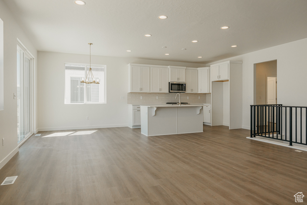 Kitchen with stainless steel microwave, light wood-style flooring, backsplash, white cabinets, and a chandelier